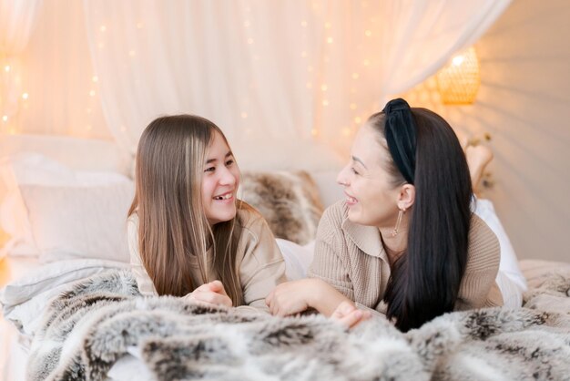 Mamma e figlia felici si abbracciano sul letto in una camera da letto decorata la vigilia di Natale in attesa del