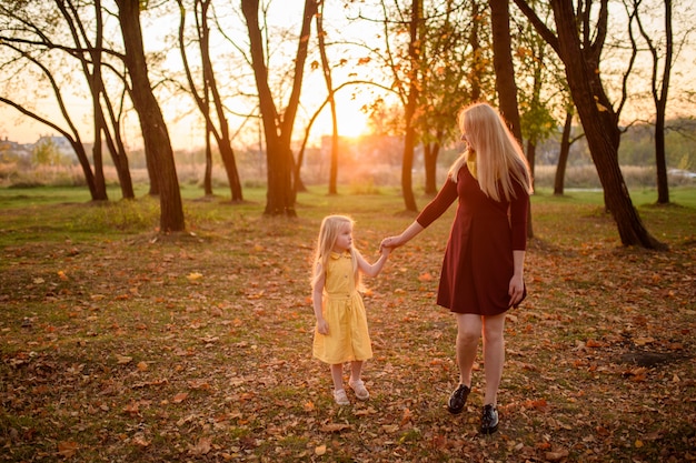 Mamma e figlia in abiti camminano per mano nel parco d'autunno.