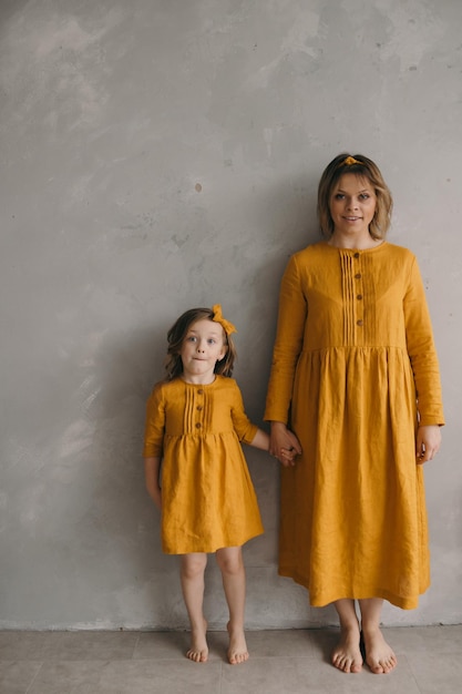 Mamma e figlia in bei vestiti gialli sono in piedi vicino al muro strutturato che si abbracciano divertendosi