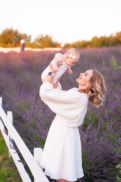 Mamma e figlia in bellissimi abiti bianchi in un campo di lavanda in estate al tramonto.