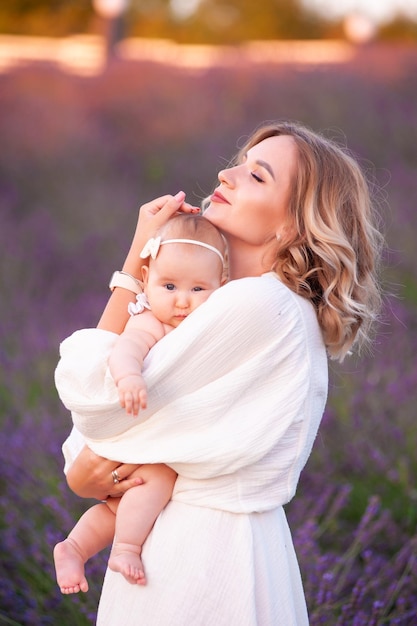 Mamma e figlia in bellissimi abiti bianchi in un campo di lavanda in estate al tramonto.