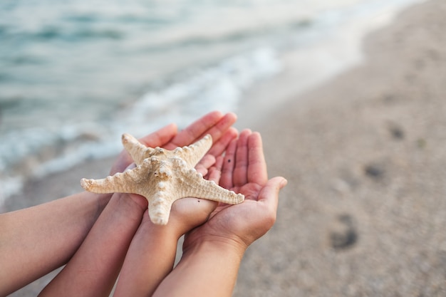 Mamma e figlia nelle mani che tengono una stella marina sullo sfondo del mare