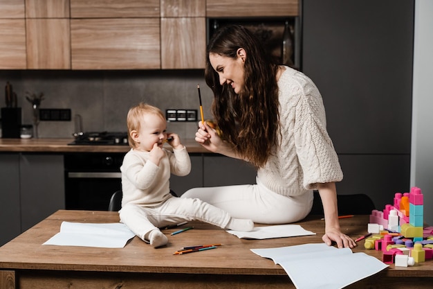 Mamma e figlia scherzano e giocano insieme in cucina a casa La famiglia felice di mamma e figlia ride e gioca con le matite colorate mentre disegna Congedo di maternità