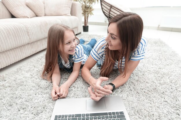 Mamma e figlia sdraiate sul tappeto e utilizzando un laptop