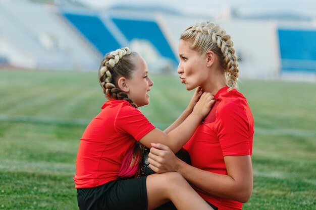 Mamma e figlia sono sedute in abiti sportivi sul campo di calcio e si abbracciano