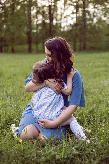 Mamma e figlia sono sedute su un prato verde in abiti blu