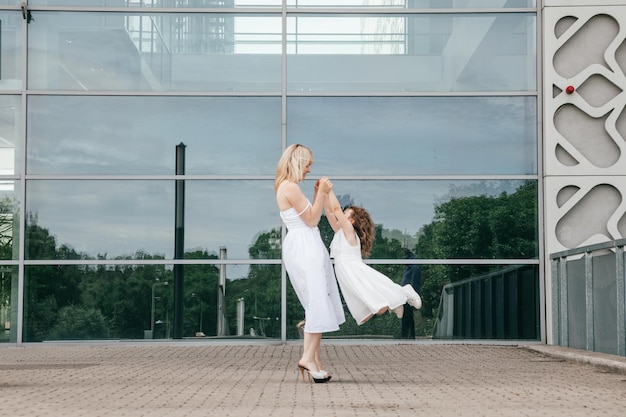 Mamma e figlia vestite con abiti di cotone bianco a piedi in città il giorno d'estate. Relazione felice. Infanzia meravigliosa. Gente meravigliosa. Gioia e avventura. Modello di ruolo. Materiali naturali.