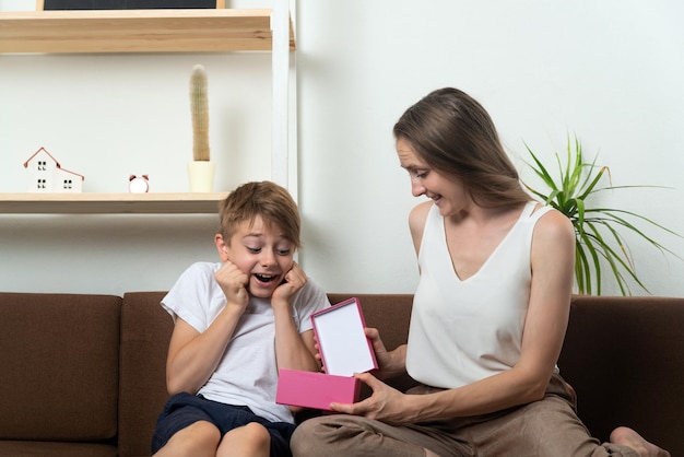 Mamma e figlio aprono la confezione regalo seduti sul divano Festa di famiglia