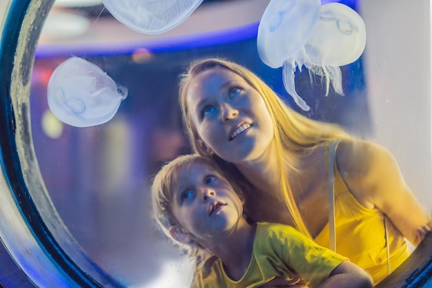 Mamma e figlio che guardano le meduse su sfondo blu in acquario