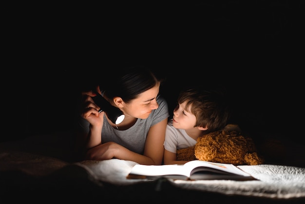 Mamma e figlio che leggono un libro con una torcia sotto la coperta