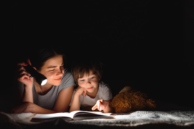 Mamma e figlio che leggono un libro con una torcia sotto la coperta