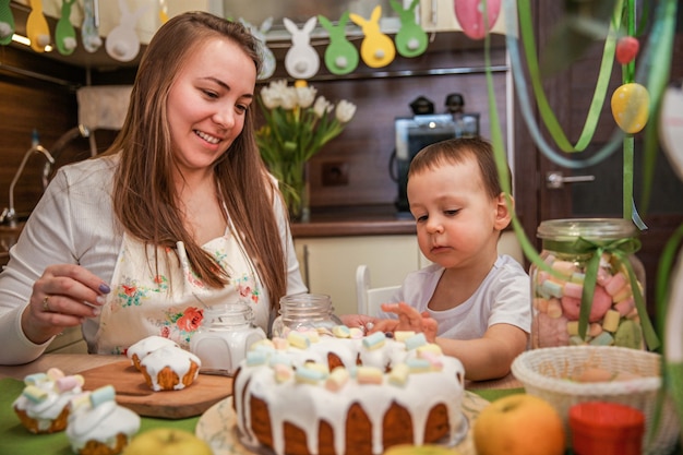 Mamma e figlio piccolo decorano i dolci pasquali a casa al tavolo della cucina decorata