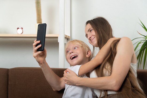 Mamma e figlio si abbracciano e si fanno selfie sul loro smartphone a casa sul divano.