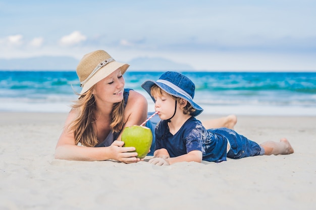 Mamma e figlio si godono la spiaggia e bevono cocco.