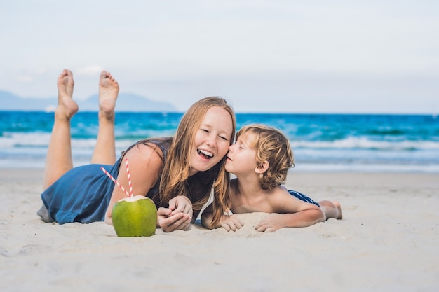 Mamma e figlio si godono la spiaggia e bevono cocco.