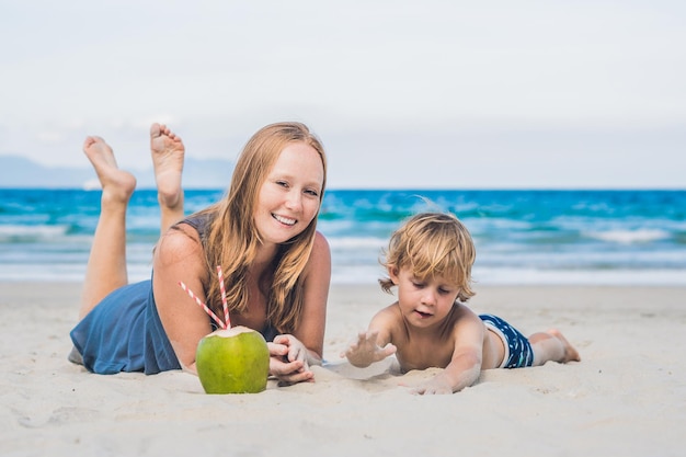 Mamma e figlio si godono la spiaggia e bevono cocco