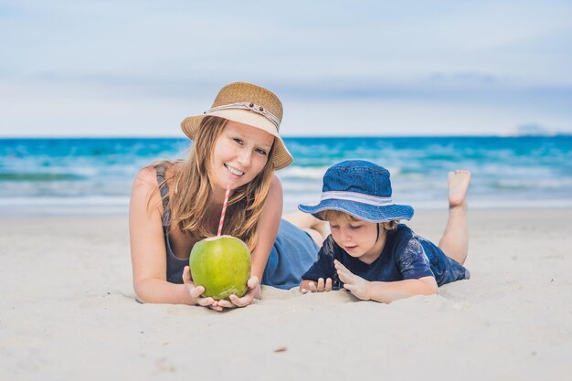 Mamma e figlio si godono la spiaggia e bevono cocco.