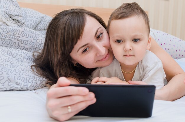 Mamma e figlio si trovano sul letto della casa e guardano i cartoni sul tablet