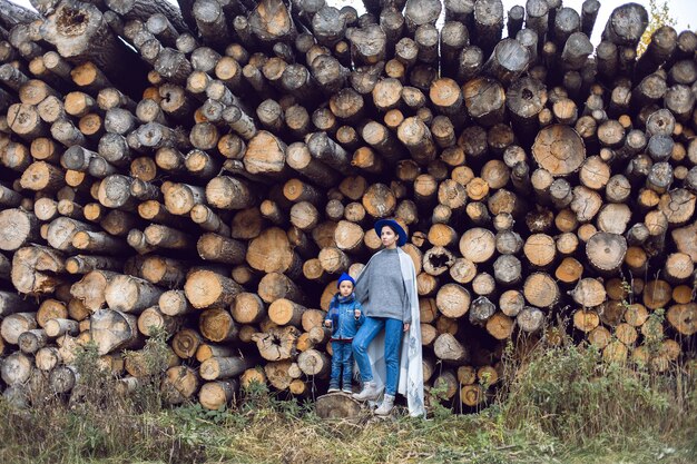 Mamma e figlio sono in piedi vicino ai tronchi della segheria in autunno