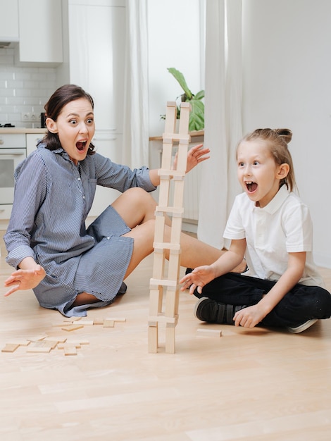 Mamma e figlio sorpresi che guardano la torre jenga cadere di lato Giocando sul pavimento