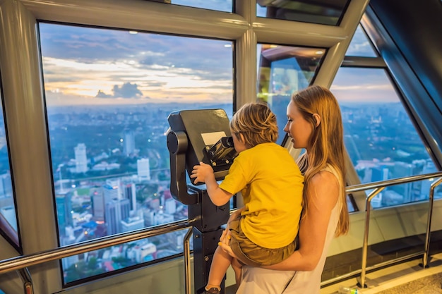 Mamma e figlio stanno guardando il paesaggio urbano di Kuala Lumpur Utilizzare il binocolo Vista panoramica dello skyline della città di Kuala Lumpur sera al tramonto grattacieli in Malesia Viaggiare con il concetto di bambini