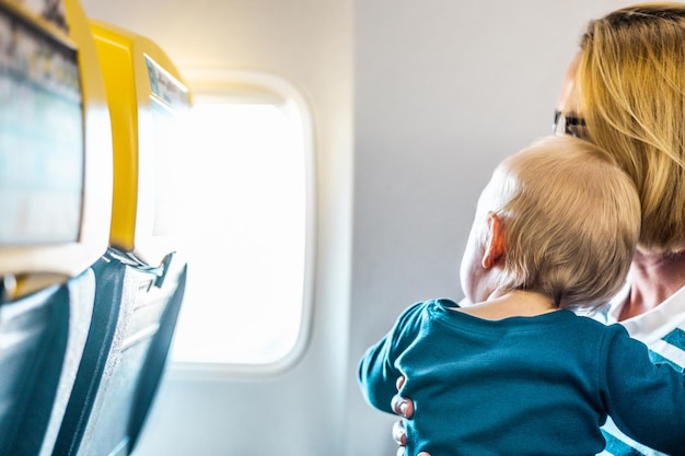 Mamma e figlio volano in aereo Madre che tiene e gioca con il suo bambino bambino ragazzo nel suo grembo durante il volo economico commerciale Foto concettuale di viaggio aereo con bambino Persone reali