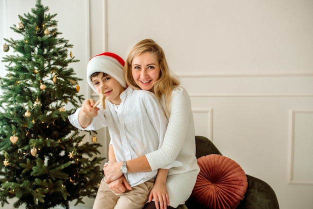 Mamma e Herson giocano sdraiati nel soggiorno di Natale. Decorano un albero di Natale in legno con luci