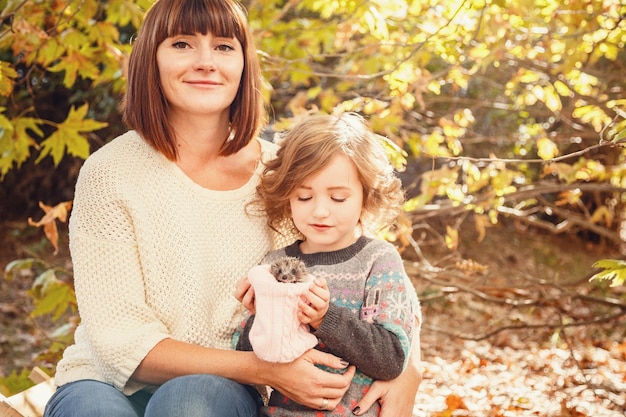 Mamma e le sue figlie sono trattenute da un piccolo riccio Autunno toccabile che dipinge le foglie autunnali gialle sullo sfondo