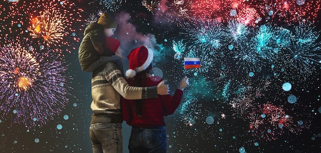 Mamma e papà con il figlio sulle spalle in abiti caldi e con un cappello da Babbo Natale La famiglia festeggia il nuovo anno guardando i fuochi d'artificio fuori