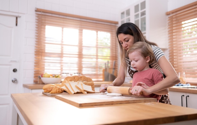 Mamma e papà nella cucina di casa con i loro bambini piccoli Divertitevi a cuocere il pane ea preparare la cena insieme