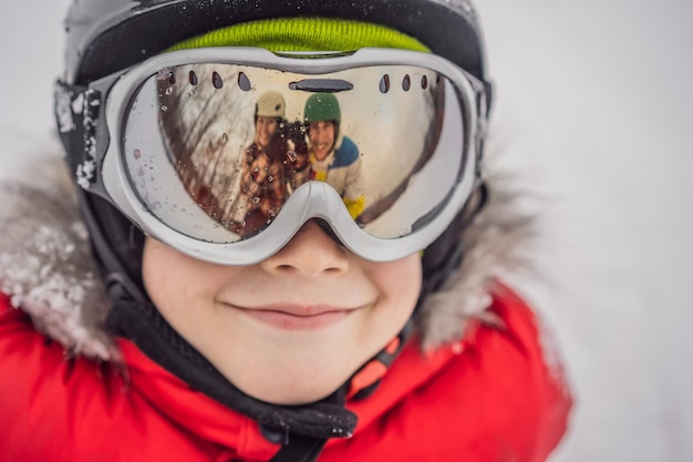 Mamma e papà si riflettono negli occhiali da sci del ragazzo Mamma e papà insegnano a un ragazzo a sciare o fare snowboard