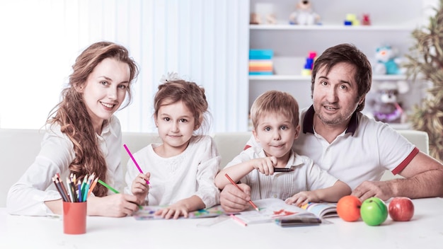 Mamma e papà stanno dipingendo con i bambini seduti al tavolo della scuola materna