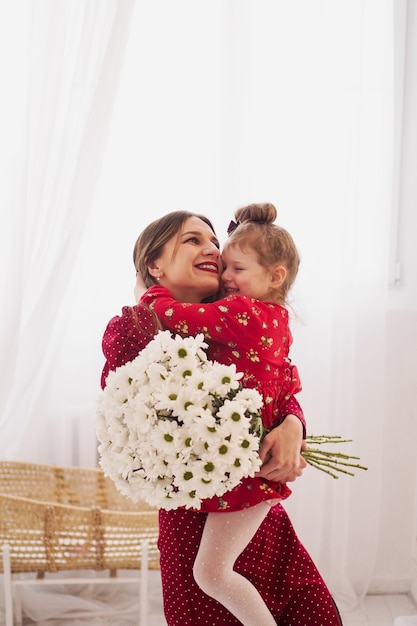 Mamma e piccola figlia in abiti rossi in una luminosa camera da letto