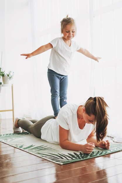 Mamma felice e figlia piccola che fanno esercizio mattutino insieme nella luminosa casa interna