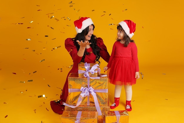 mamma figlia in un vestito rosso in un cappello di babbo natale scatole regalo coriandoli concetto di capodanno