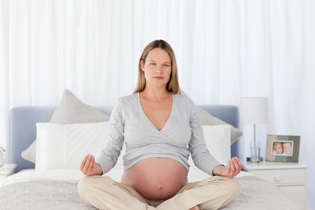 Mamma futura seria che fa meditazione su un letto