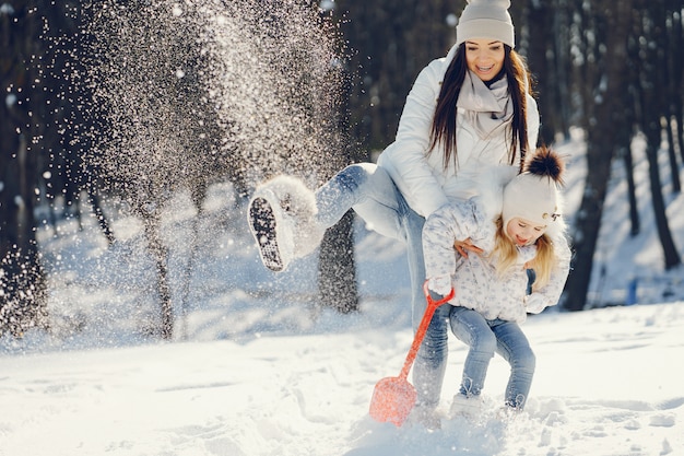 mamma giovane e alla moda che gioca con la sua piccola figlia carina nel parco di neve invernale