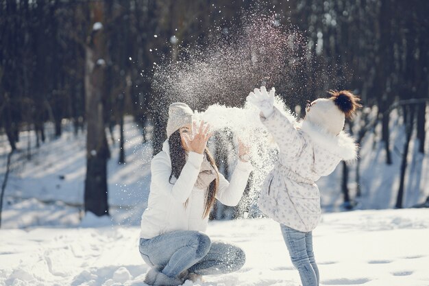 mamma giovane e alla moda che gioca con la sua piccola figlia carina nel parco di neve invernale