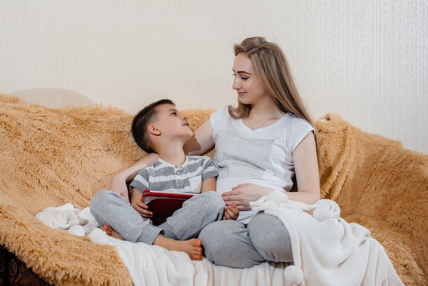 Mamma incinta gioca con suo figlio sul divano nel tablet. Cura, famiglia, amore