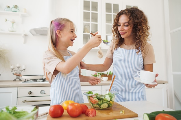 Mamma insegna a sua figlia adolescente a cucinare insalata di verdure in cucina