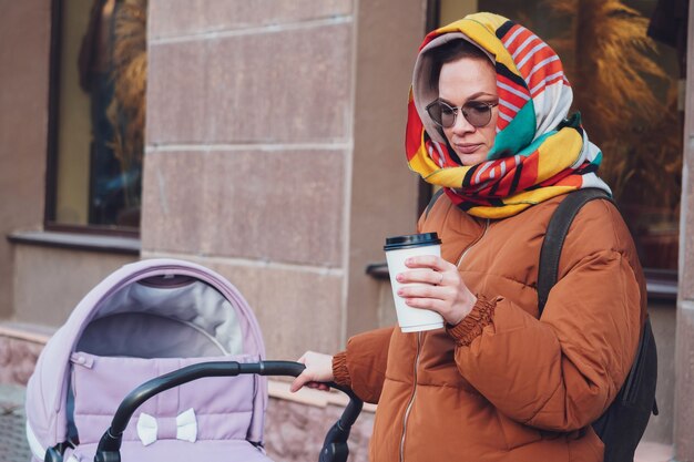 Mamma moderna alla moda con un passeggino in una passeggiata in città, autunno