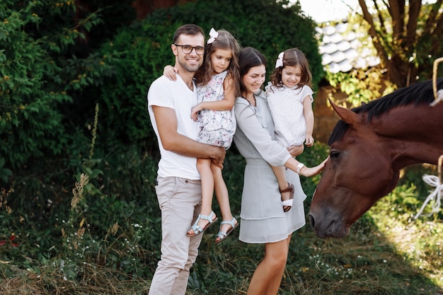 Mamma, papà che abbraccia le figlie si divertono a camminare nella fattoria e guardare il cavallo. Giovane famiglia trascorrere del tempo insieme in vacanza, all'aperto.