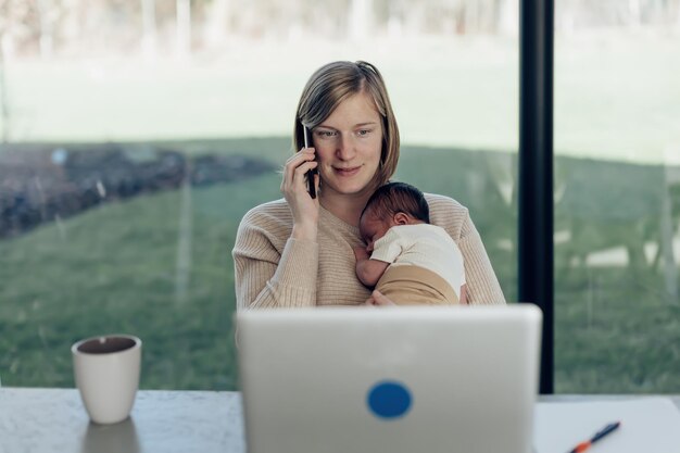 Mamma seduta davanti al computer portatile che tiene il lavoro a distanza del bambino da casa