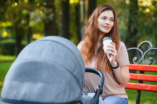 Mamma seduta su una panchina. Donna che spinge il suo bambino seduto in una carrozzina. Concetto di famiglia.