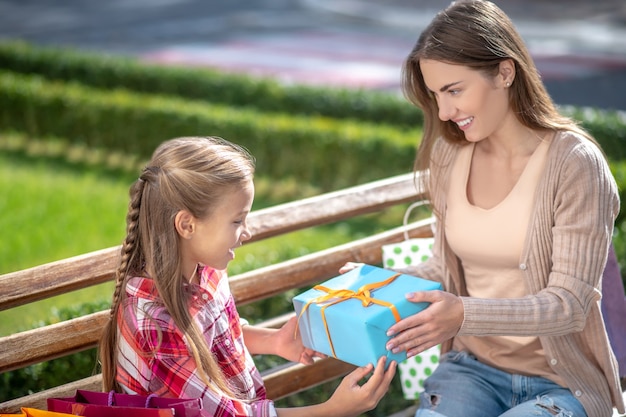 Mamma sorridente che dà il contenitore di regalo della figlia sulla panchina del parco