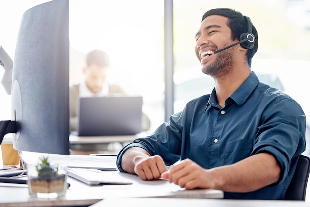 Man laugh and computer with headset in office for support customer with problem in Turkey Male consultant keyboard and help with headphones for telemarketing service for debt review or loan