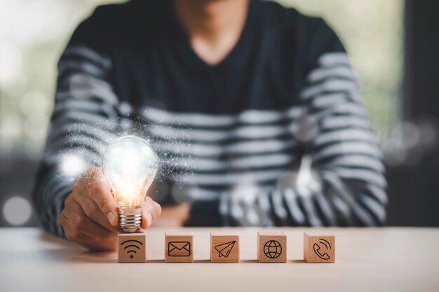 Man mano che tiene la lampadina con l'icona Business sul cubo di legno e lavorare sulla scrivania, creatività e innovazione sono le chiavi del successo. Concetto di nuova idea e innovazione con Brain e lampadine.