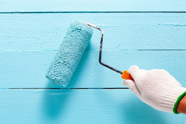 Man mano che tiene la spazzola a rullo di vernice di colore blu su sfondo di parete di colore di legno blu