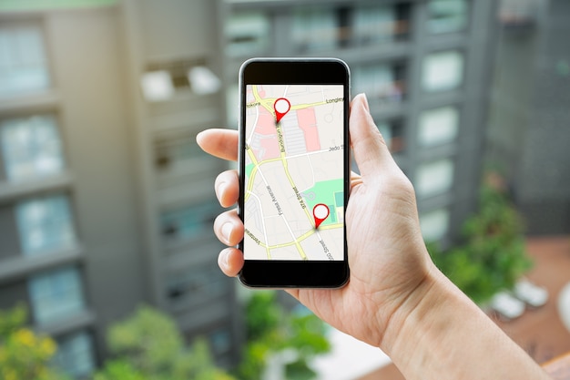 Man mano che tiene smartphone con mappa GPS per instradare la connessione di rete di destinazione. Posizione Mappa stradale con icone GPS Navigazione e icona rossa della posizione. Concetto di navigazione in linea.