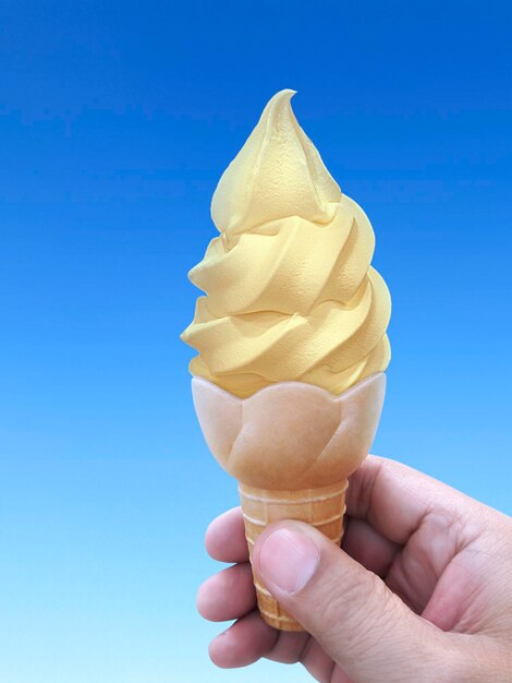 Man mano che tiene un cono gelato su sfondo il cielo blu